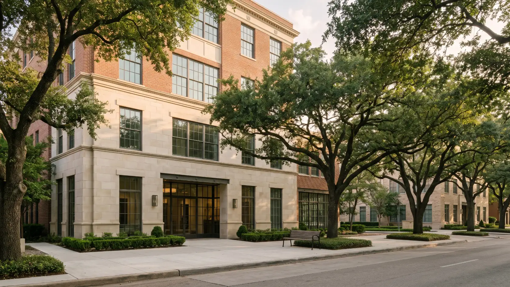 A limestone and brick building on a Houston street shaded by live oaks